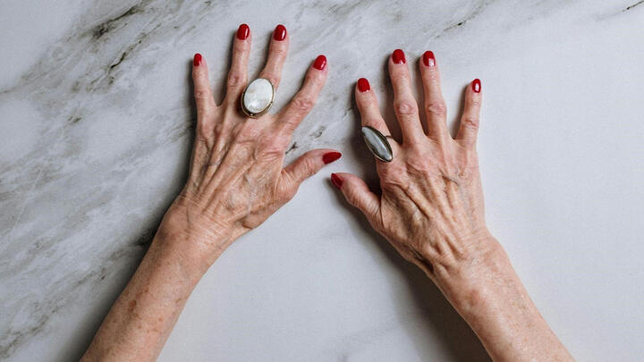 Old female hands with red nail polish and rings on a marb